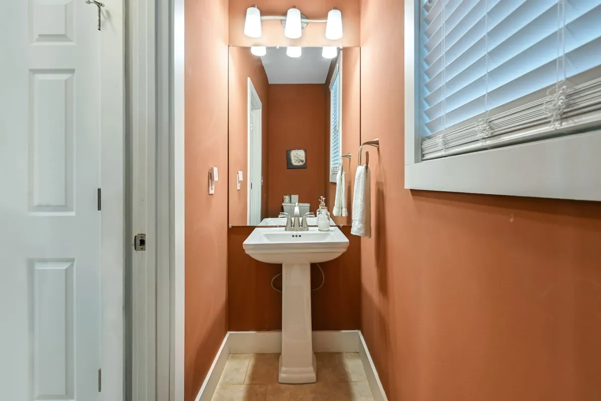 A compact and stylish half bath featuring a pedestal sink, mirrors, elegant light fixtures, and a towel holder. The space is both functional and welcoming, ideal for guest use during social gatherings.
