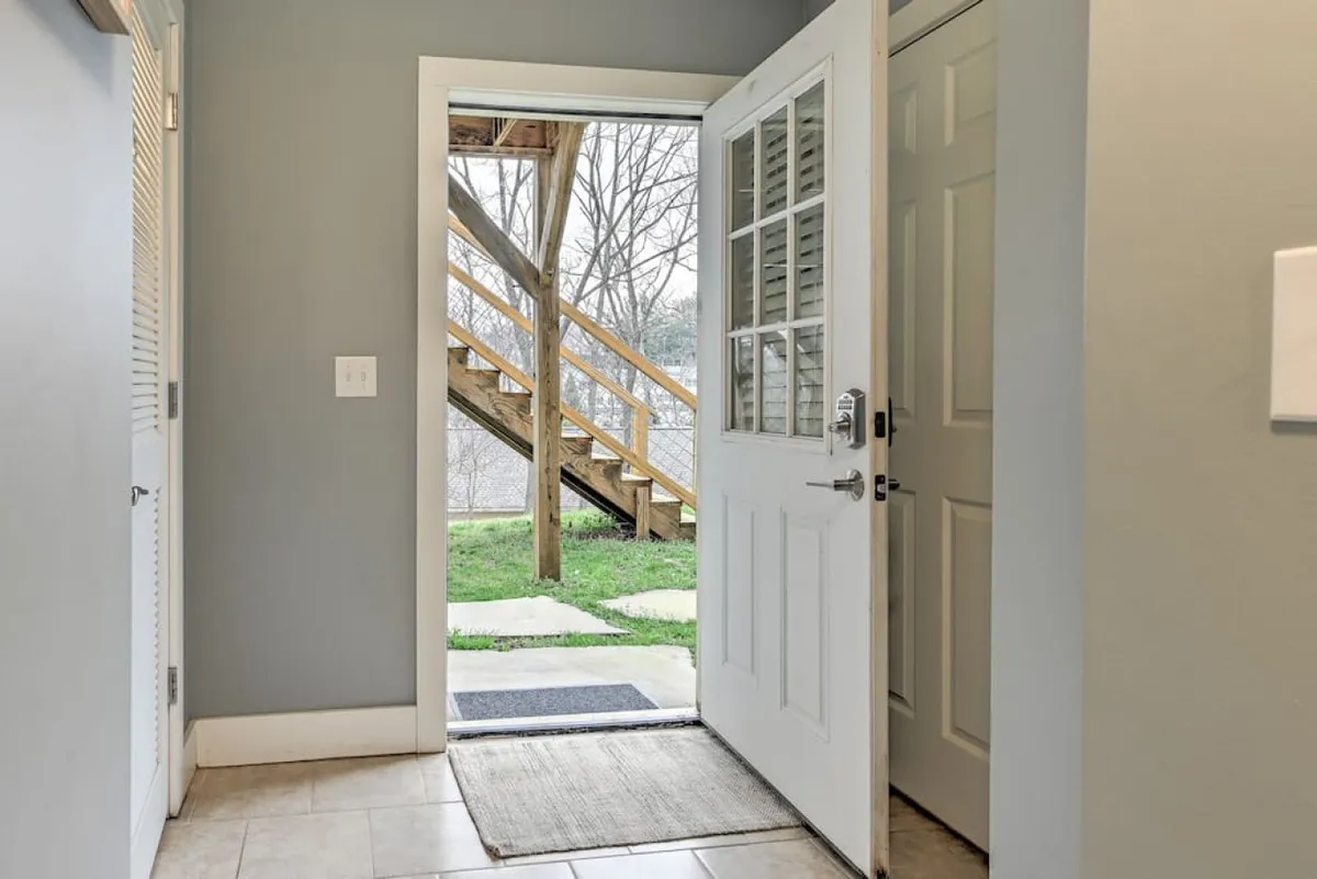 The photo captures the open front door leading to a green lawn, with a welcoming entryway and a glimpse of the staircase inside. Natural light suggests a pleasant, inviting atmosphere, and the connection between indoors and outdoors is clearly visible.