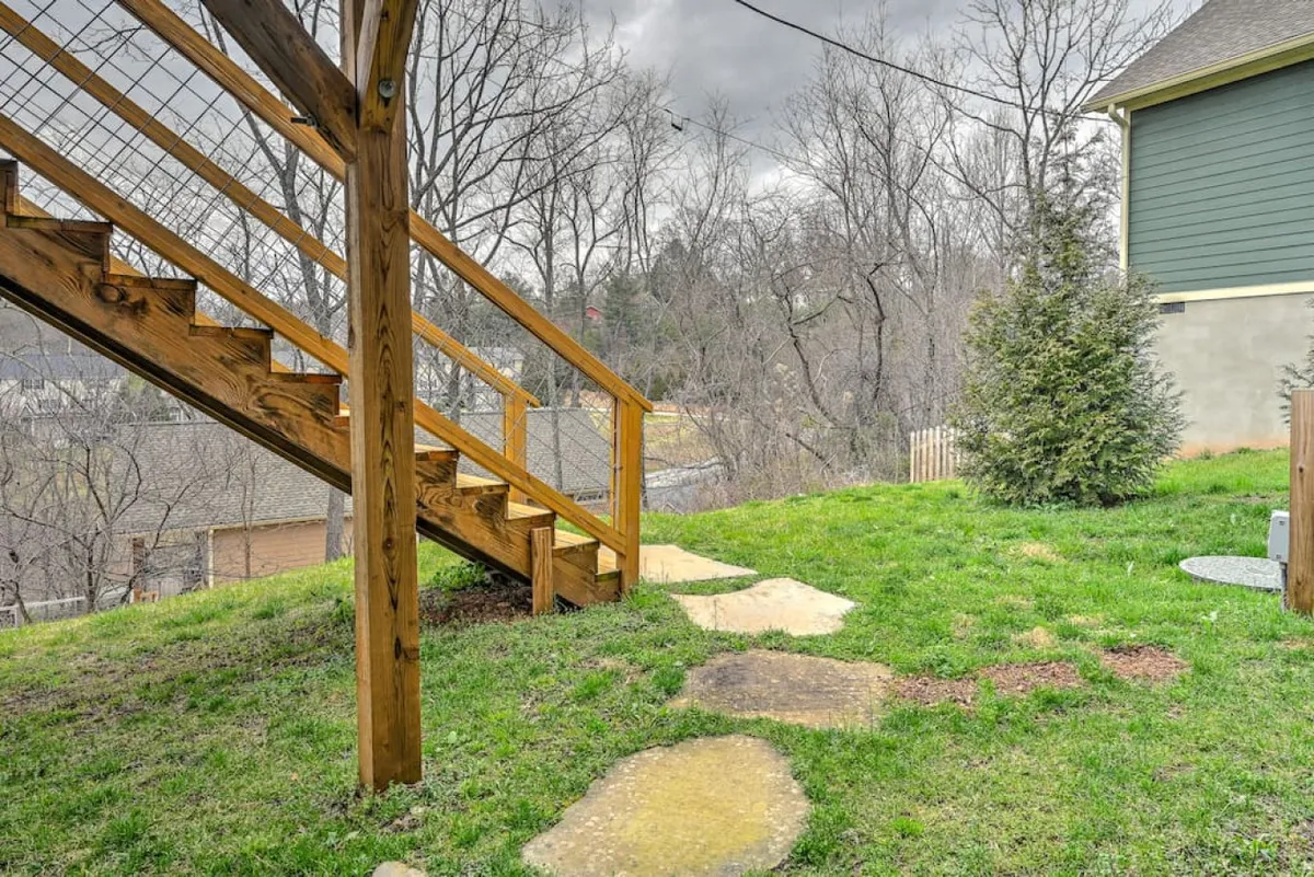 A serene backyard scene with wooden stairs leading to a stone pathway, surrounded by green grass and mature trees. The setting suggests quiet exploration, nature walks, or simply enjoying peaceful moments outdoors, echoing the area's natural attractions.