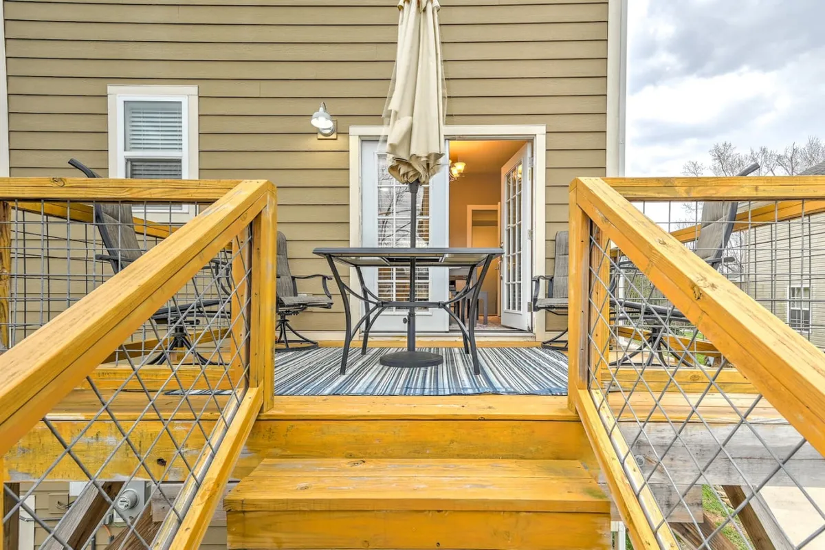 This image displays a wooden deck equipped with an outdoor table and parasol, connected to the interior by a doorway. The space is designed for al fresco dining, relaxing under the sun, and socializing, evoking the spirit of casual family meals and starlit conversations.