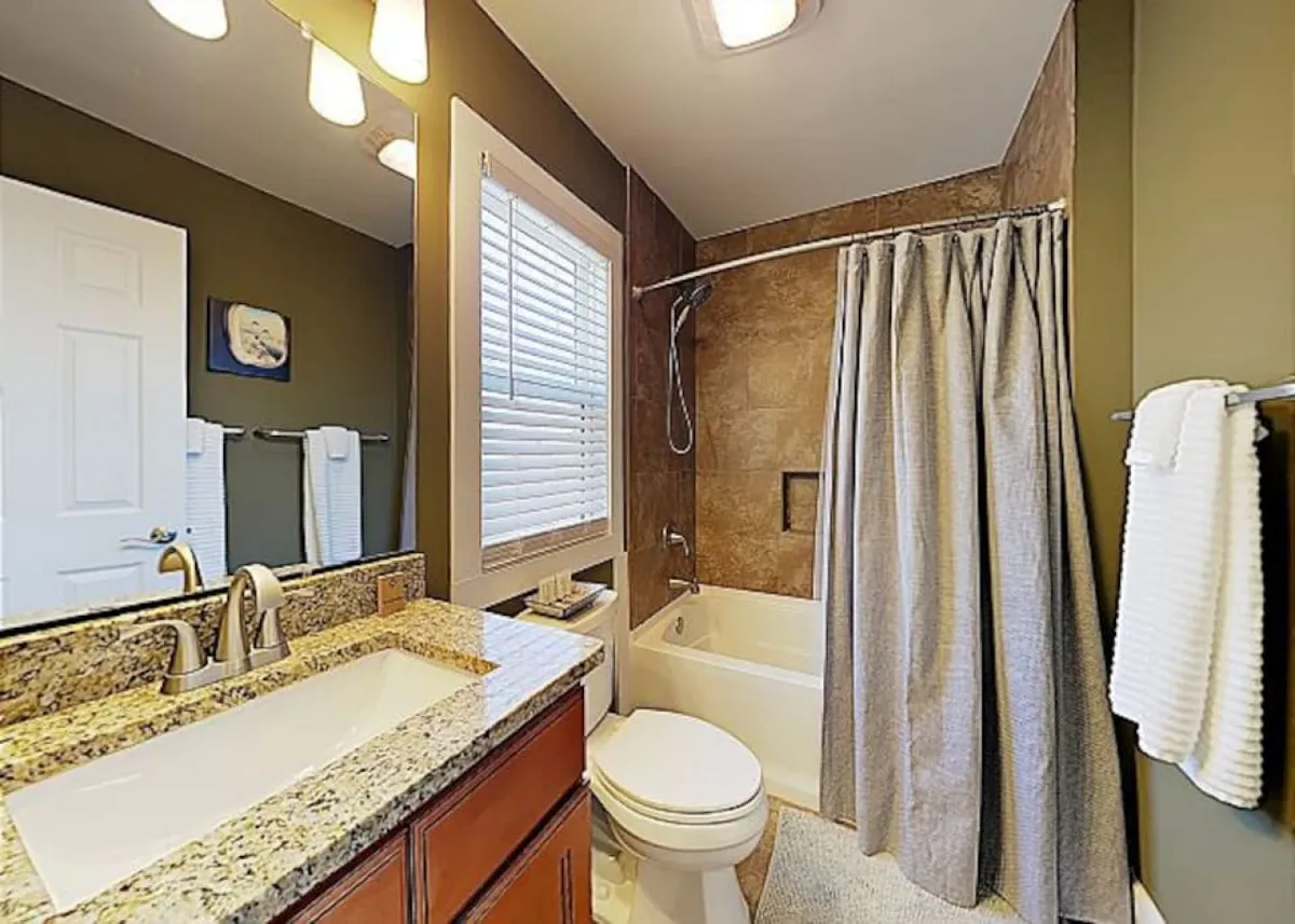 A serene bathroom featuring a granite countertop, bathtub, shower area, and vanity mirror. The space is designed for relaxation and personal routines, suggesting the ensuite and shared bathroom amenities available to guests.